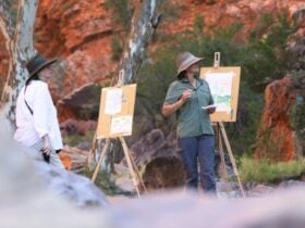 two women stand at easels painting outdoors