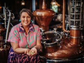 A woman standing in front of a copper distiller with native botanical fruit in her hands