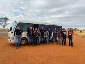 a group of people standing by a bus that is parked on red sand