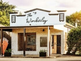 Street View and facade of brick building with decorative parapet and signage reading The Wimberley