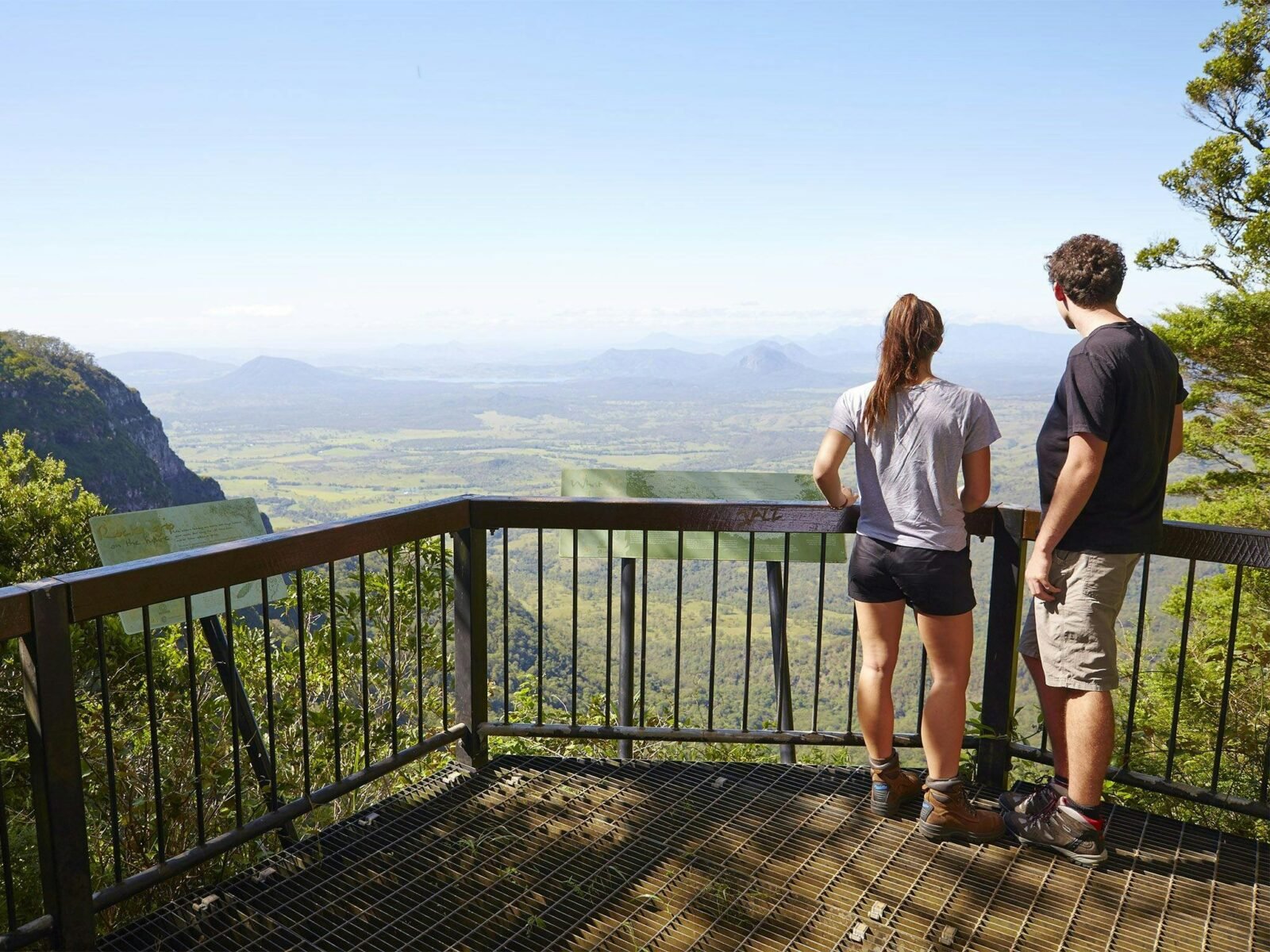 Two people standing at a lookout looking over and valley and mountains in the distance.