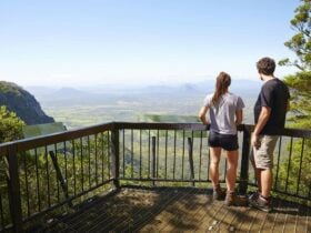 Two people standing at a lookout looking over and valley and mountains in the distance.