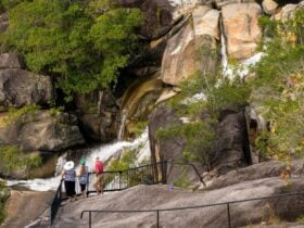 Three people standing at granite rock lookout watching a waterfall.
