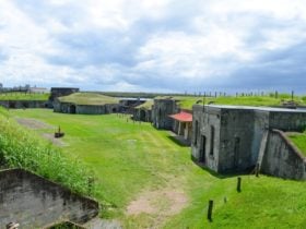 Fort Lytton buildings with grassy surrounds and cloudy sky.