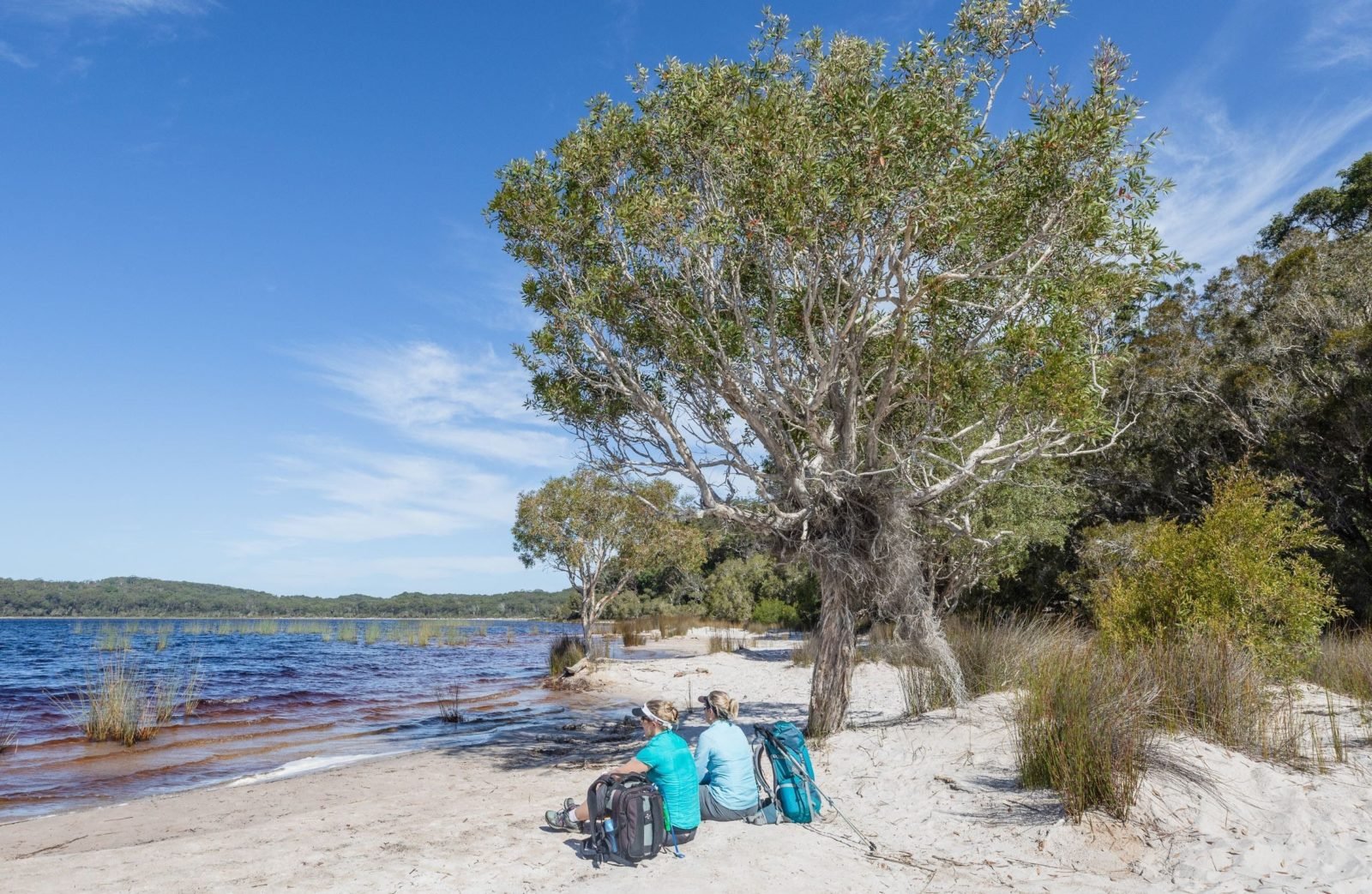 photo showing two hikers sitting on a sandy beach at Lake Birrabeen