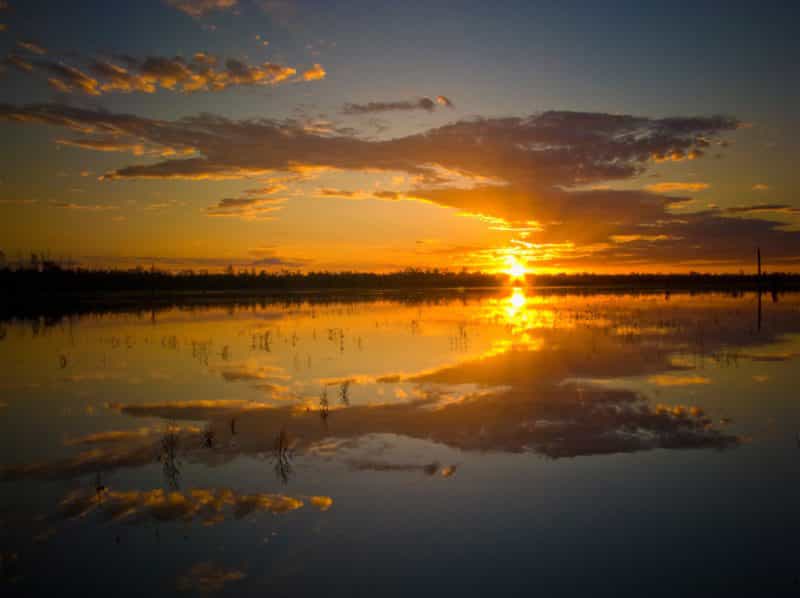 Orange sun setting over water with reflection.