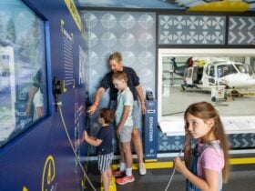 A mother and three children engaging with interactive exhibits with a helicopter in the background