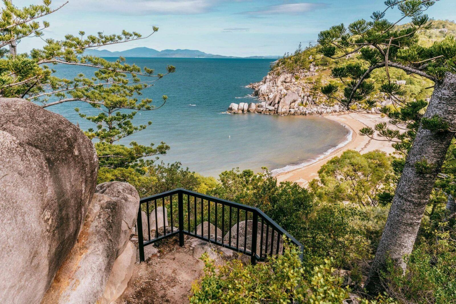 Looking down on a bay with hoop pine-clad granite headland and ocean and mountains in the background