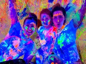 A family of two adults and one child with thei hands in the air covered in glowing paint
