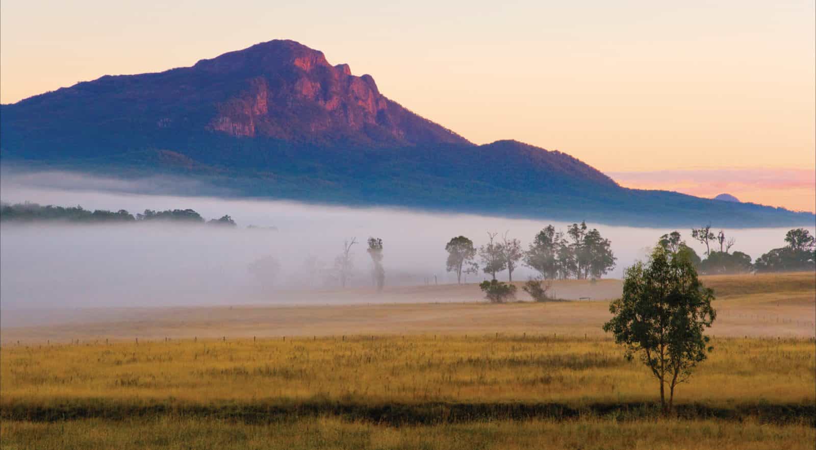 Mount Maroon with base shrouded in fog and farmlands in foreground.