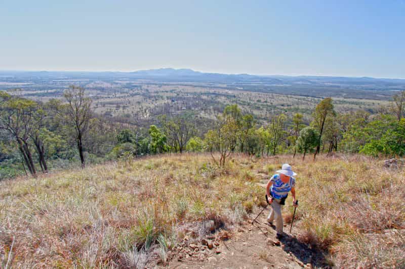 Walker on a track strides up a mountain slope with mountains and valleys in the distance.