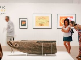 two women inspect a wooden carved sculpture of an indigenous fish god