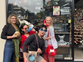 Staff posing outside the store with fun handbags, a skull, oversized flower hat & Chill Pill pillow