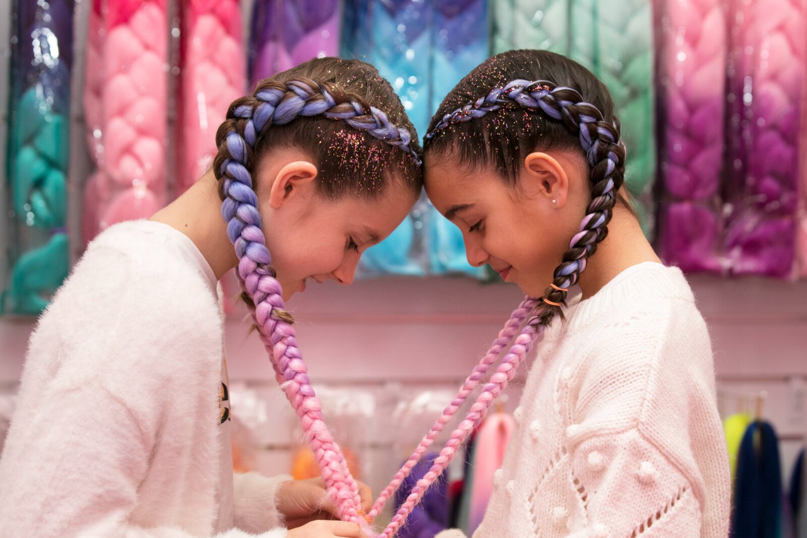 two girls with their heads together and their hair braids are forming a love heart shape