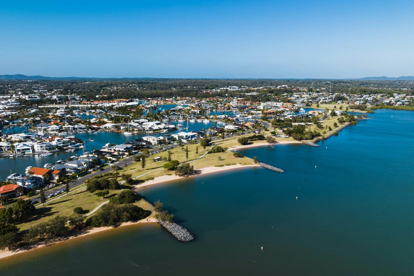 Aerial view of Raby Bay Foreshore Park, surrounded by housing, clear blue skies and canals.