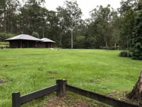 Shelter shed sits in grassy open space fringed by forest.