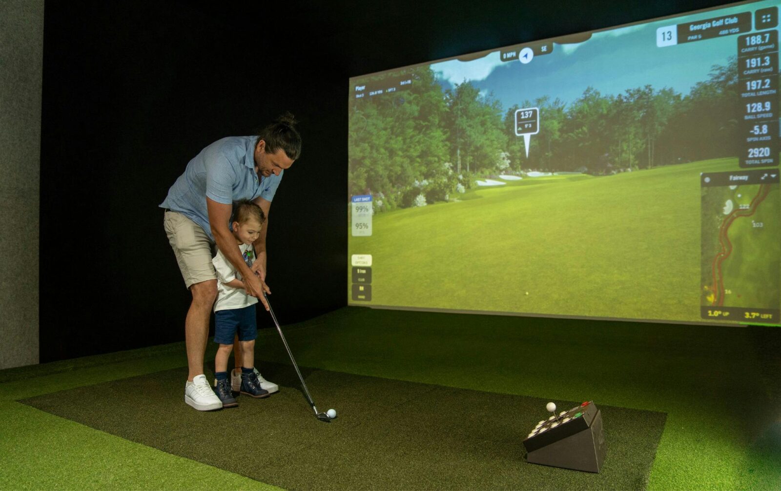 A father teaches his young son how to putt using the golf simulator