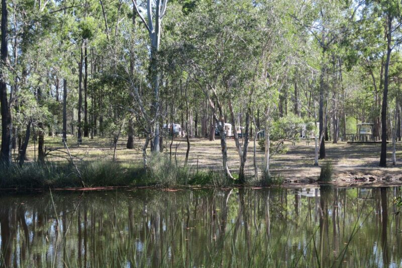 Looking across waterhole at camping area with two caravans.