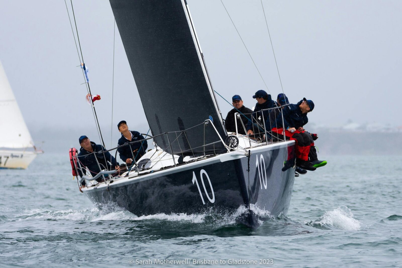 Sailors sitting along the edge of a yacht with black sails as it races through the water.