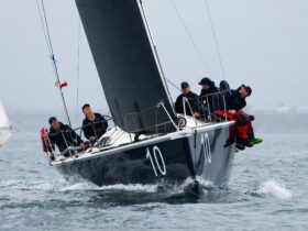 Sailors sitting along the edge of a yacht with black sails as it races through the water.