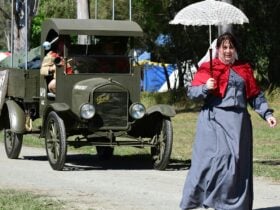 A lady dressed as a WW1 Nurse with a parasol leads a WW1 Vehicle