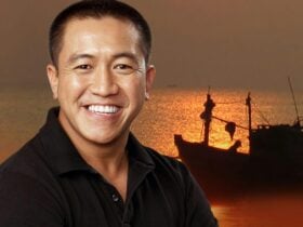 Anh Do standing in front of a refuge boat with sun setting on water