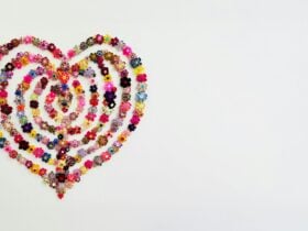 Heart-shaped spiral of colourful handmade fabric flowers on a plain white background