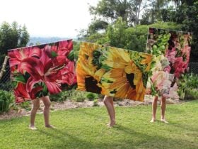3 people holding 3 large paintings of different flowers
