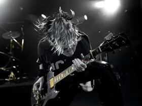 Sarah McLeod of The Superjesus on stage, leaning towards the camera, playing a Gibson guitar