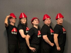 Five caucasian men of varying ages dressed in black t-shirts with red traffic cone style hats
