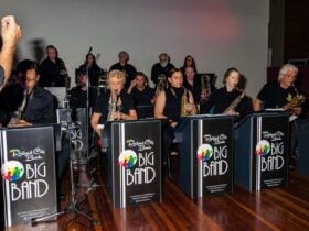 13 members of brass band in picture, with front row of 5 saxophonists playing their instruments