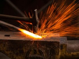 Hammer striking heated metal on anvil creating sparks.