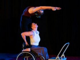 Woman in a wheelschair holds the feet of a woman standing on wheelchair wheels and bending backwards