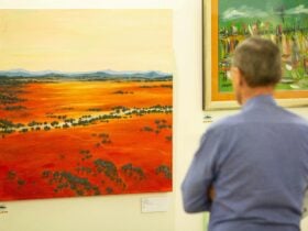 A man in a long sleeved blue shirt observes a landscape piece on canvas