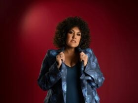 Casey with curly hair and hands on collar of shirt