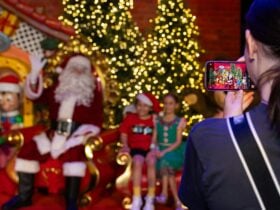 Santa waves on a golden throne with kids; a phone captures the festive tree and holiday scene.