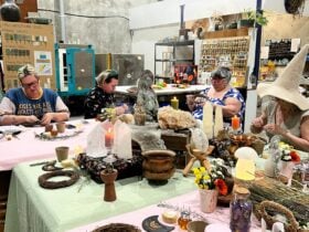 A group of participants sit around tables covered with pink and green cloths, crafting and working