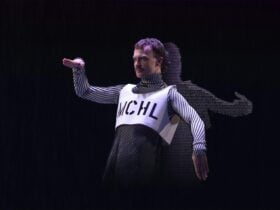 A male dancer poses in a robotic position. His shadow is filled with coloured text.