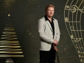 A middle aged man in suits holding a guitar against Christmas background.