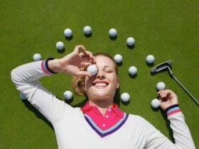 A person laying down on a golf green with golf balls surrounding their head.