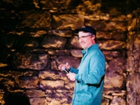 Comedian Stu Daulman on stage at a comedy club, with a dimly backlit heritage brick wall behind him