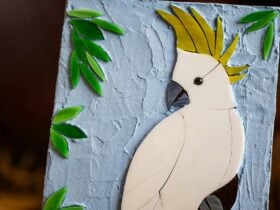 Glass mosaic of cockatoo with sky and leave background.