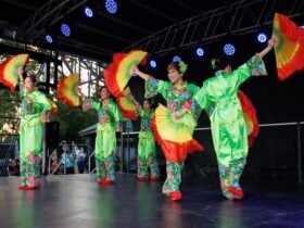 Cultural performance on stage of ladies in green costumes with rainbow fans