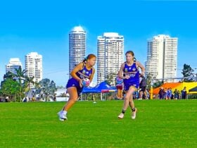 Young female touch players on a grassy field with the Gold Coast city skyline in the background