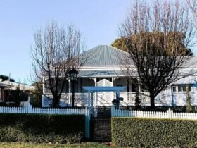 An old white cottage behind a hedge and white picket fence