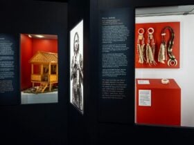 A dark gallery space with illuminated portraits of women holding sentimental objects and object case