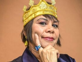 Toni Janke wearing a golden crown with ornate details and yellow gemstone earrings