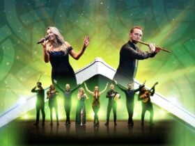 Performers sing, play instruments, and dance on a glowing stage with a vibrant green background