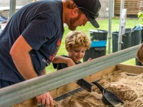 A boy excavates an artefact from the Archaeological Dig with his father