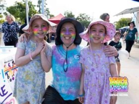 Young rainbow family smiling for the camera with rainbow face paint at Loud and Proud Logan
